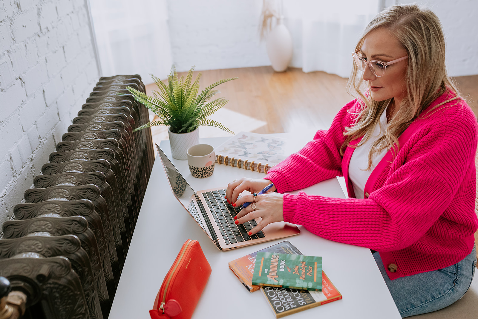 CPA for Photographers Jamie Boyack from Aloha Friday CPA sitting at a desk typing on the computer while wearing a pink sweater and glasses