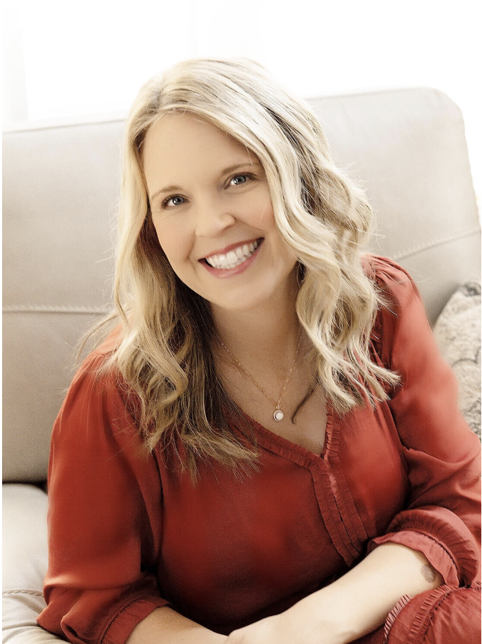 A woman with wavy blonde hair is sitting on a beige couch, smiling. She is wearing a rust-colored blouse and a necklace, with a soft-focus background adding a warm, relaxed atmosphere. She is promoting black friday deals for photographers 