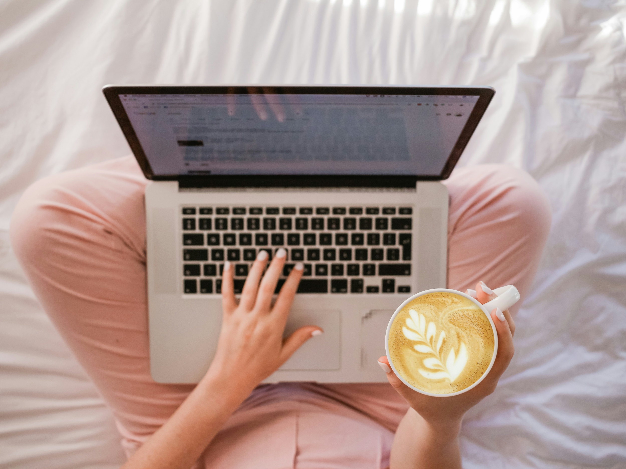 A look down into the lap of a woman with a coffee working on a computer to outsource blog writing
